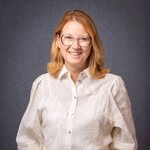 Smiling blond woman wearing glasses and white blouse on gray backdrop