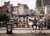 Two people sitting on railing overlooking dense urban skyline of mixed old and new buildings.