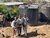 Three people smiling beside two large black water tanks in a rural setting
