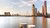 Two wooden mooring posts in calm river with modern city skyline and cable-stayed bridge at dusk