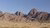 Panoramic view of reddish rocky hills under clear blue sky and a single industrial chimney smoking 