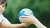 Child’s hand reaching for a globe held by adult hands against blurred green foliage