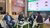 Four people seated at green-carpeted conference booth discussing in front of a sustainability slide