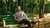 Man in striped shirt relaxing on green bench in sunlit woods