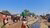 People walking past corrugated tin shacks under clear blue sky along dusty street with open drainage