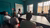 Eight individuals seated around a table in a teal room watching a presentation.