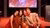 Five smiling people, including a child, on a graduation stage lit red in front of a large screen.