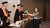 Woman in blouse receives green diploma tube from academic in black-orange gown at ceremony