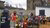 Aid workers distributing meals to a group of children in a courtyard with old buildings.
