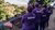 Four people in purple Kaloola shirts and caps stand on a rooftop overlooking hillside homes.