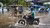 Motorcyclists and a bicyclist splashing through floodwater on a city street