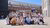 About 40 smiling people posing on sunny courtyard with historic brick buildings behind them