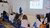 instructor pointing at projected slide as seated participants watch in a white room